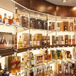 A well-lit shop showcasing a variety of spirits, including whiskey, vodka, and wine. Shelves with Bright Green technology LED shelf lighting and tables are stocked with bottles, boxes, and gift sets.