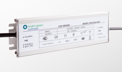 A rectangular silver-colored LED driver with a detailed label on the front. The label includes "Bright Green Connect" logo, model number PXS-24V-024, input/output specifications, safety certifications, and wiring info. Several wires protrude from both ends.