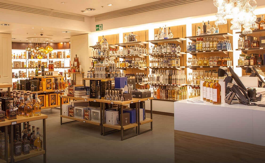A well-lit shop showcasing a variety of spirits, including whiskey, vodka, and wine. Shelves with Bright Green technology LED shelf lighting and tables are stocked with bottles, boxes, and gift sets.