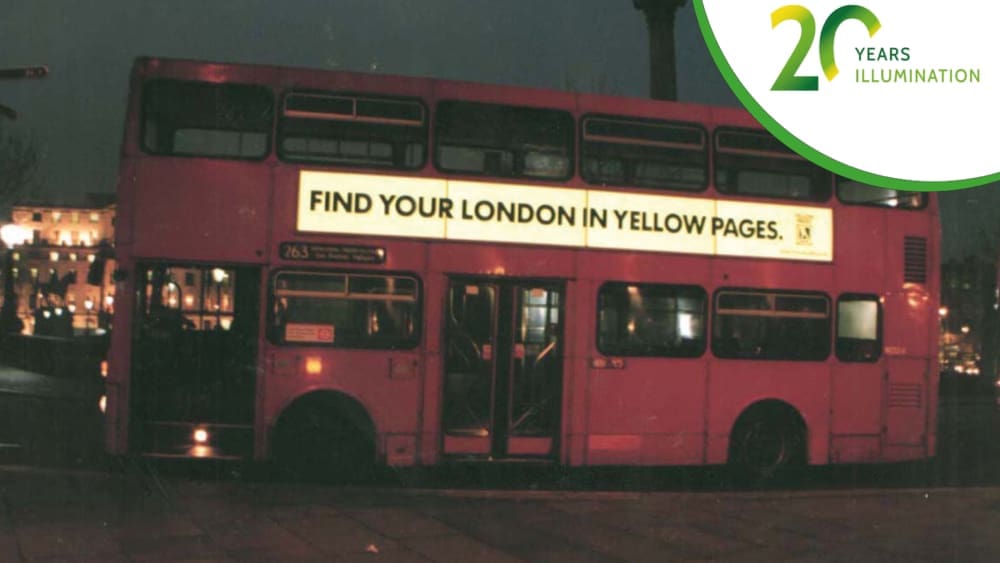 A classic red double-decker bus in London at night features an illuminated advertisement on the side that reads, "Find your London in Yellow Pages." Celebrating "20 Years of Illumination".